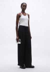 Fehér trikó, derékban magasított fekete széles szárú nadrág, fekete cipő, áttetsző kézitáska. Sima textúrák, minimalista design, semleges színpaletta.