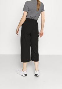 Black cropped pants with a loose fit and elastic waistband, paired with a striped short-sleeve top. Shoes are light-colored sneakers.