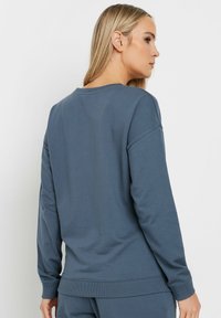 Sudadera gris de manga larga con cuello redondo, puños acanalados y un corte holgado, fabricada con un tejido suave y de textura lisa.