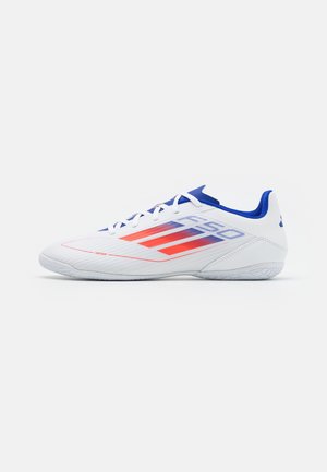 Chaussure de sport blanche avec intérieur bleu et bandes graphiques rouges et bleues sur le côté, montrée de la face externe sur un fond blanc.