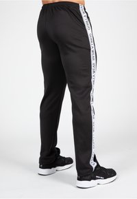 Zwarte joggingsbroek met een taps toelopende fit, voorzien van witte logotape langs de zijkanten. Gemaakt van zachte stof met een elastische tailleband en afgeknipte onderkanten.