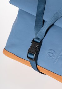 Borsa di stoffa blu con una base beige, caratterizzata da una tracolla con fibbia nera e superficie testurizzata. Leggero dettaglio del logo impresso sul lato.