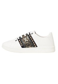 Zapatilla baja blanca con franjas decorativas metálicas doradas y negras en los laterales, tachuelas doradas redondas, suela blanca plana y cordones blancos.