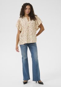 Bluse mit floralem Muster, kurzen Ärmeln und einem Ausschnitt, kombiniert mit ausgestellten blauen Jeans und schwarzen spitzen Schuhen.
