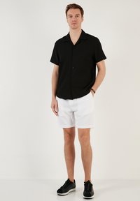 Zwart kortebloushemd met knopen en verticale strepen, gecombineerd met witte geribde shorts en zwarte sportieve sneakers.