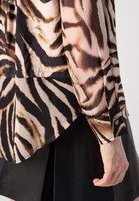 Blusa a maniche lunghe con motivo che presenta un sobrio design a strisce di tigre in nero, marrone e beige, con polsini a bottoni e una vestibilità rilassata.