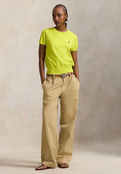 Λαχανί πλεκτό τοπ με κοντά μανίκια και ριμπ τελείωμα, συνδυασμένο με μπεζ παντελόνες φαρδιάς γραμμής. Ξεχωρίζει με μια διακοσμητική ζώνη και φλατ σανδάλια.