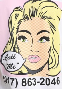 Grafisch T-shirt met een pop-art stijl blonde vrouw met groene ogen, roze lippen en een spraakbel waarin staat "Bel mij." Achtergrond is roze, met zwarte tekst eronder.