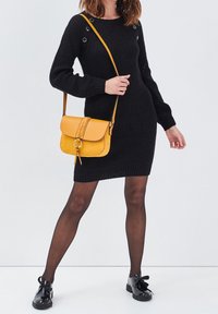 Robe en tricot côtelé noir avec de longues manches bouffantes et des détails de boutons-pression, assortie à un sac bandoulière en cuir jaune avec un rabat cousu.