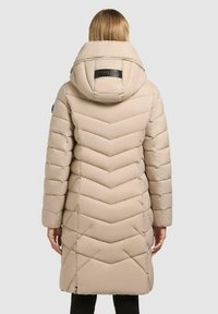 Beige vadderad jacka med ett chevronmönster, försedd med en stor huva och svart logotypdetalj på baksidan. Långa ärmar, knälång design.