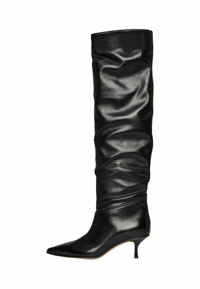 Bota de cuero negra de caña alta y estilo relajado, con punta afilada y tacón de aguja de 2 pulgadas; textura suave con tobillo ajustado y parte superior recogida.