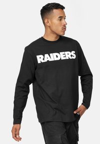 Svart långärmad t-shirt i bomull med en djärv vit "RAIDERS" grafik över bröstet. Rundad halsringning och avslappnad passform.