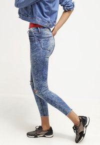 Bledé modré džíny s úzkým střihem, s vytrhanými koleny. Spárovány s černými a stříbrnými teniskami a světle modrou džínovou bundou.