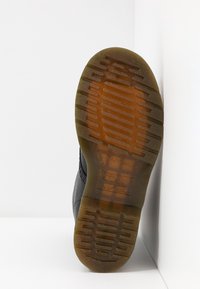 Semelle d'une botte noire avec une semelle en caoutchouc translucide brune montrant des motifs de grip texturés et des marques de la marque.
