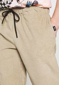 Béžové manšestrové kalhoty s ribovanou strukturou, elastickým pasem a černou šňůrkou. Obsahuje malou černou značkovou nálepku po straně.
