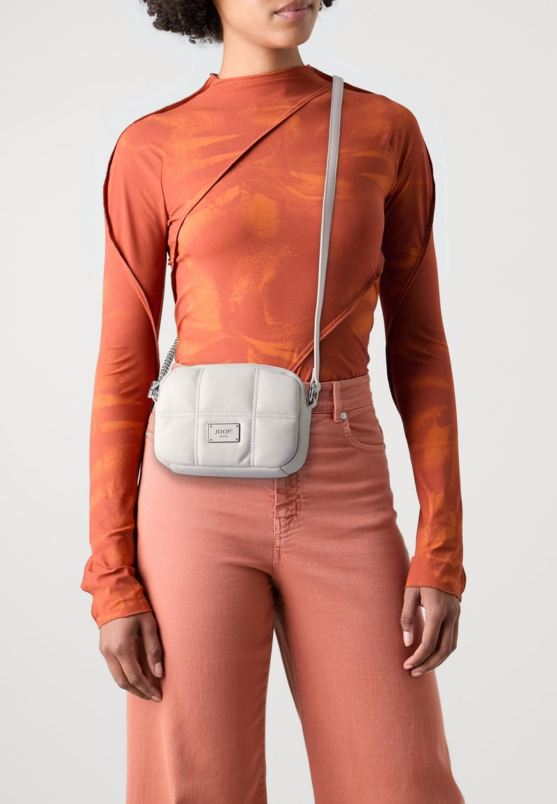 Borsa a tracolla in pelle grigia con motivo trapuntato e logo in tonalità argento. Il modello indossa un top arancione a maniche lunghe e pantaloni rosa.