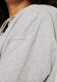 Grå pullover-tröja med ett mjukt, strukturerat tyg, utrustad med dragsko i halslinningen och en sidficka.