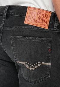 Black denim jeans featuring a prominent leather label on the waistband and contrasting white stitching with a distinct pocket design.