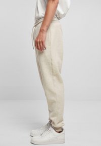 Beige katoenen joggers met een tailleband met trekkoord, zijzakken en geribbelde boorden. Gecombineerd met witte sneakers met een klein logo op het bovenbeen.