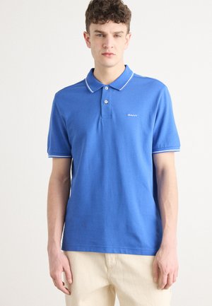 Polo bleu en coton avec un col classique, une patte de boutonnage à deux boutons et des finitions blanches contrastantes sur le col et les manches. Comprend un logo.