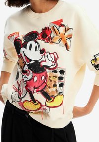 Felpa color crema con una grafica prominente di Topolino in rosso e nero, decorata con motivi floreali e astratti. Morbido al tatto, vestibilità comoda.