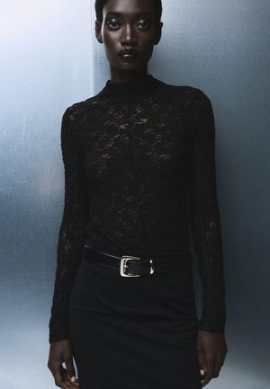 Black lace long-sleeve top with a high collar, paired with a fitted black skirt and a glossy black belt featuring a gold buckle.