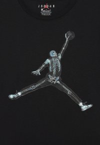 Čierne tričko s priehľadným skeletom v skákajúcej póze, ktorý drží basketbal. Potlač zobrazuje detailnú štruktúru kostí a kĺbov.