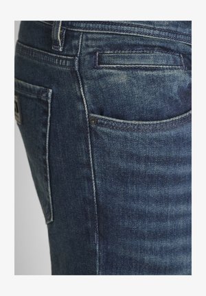 Primer plano de un bolsillo de jeans de mezclilla azul con costuras detalladas y remaches en el lado derecho.