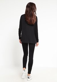 Haut noir à manches longues avec une coupe décontractée, associé à des leggings noirs et des baskets aux accents métalliques, présenté de dos.