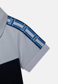 Polo shirt met een lichtgrijze body, navyblauwe onderkant en blauwgestreepte schouderdetails met 'BOSS' branding. Getextureerde stof.