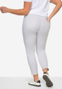 Pantalones ajustados de color gris claro con dos bolsillos traseros y cremalleras en los tobillos, combinados con zapatillas blancas que tienen un acento negro en el talón.