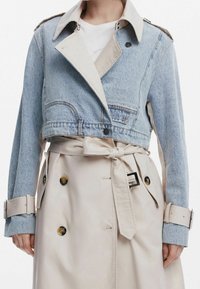 Skórzana kurtka dżinsowa z krótkim krojem w jasnoniebieskim odcieniu, połączona z beżowym trenczem z podwójnymi guzikami i przewiązywanym paskiem w talii.
