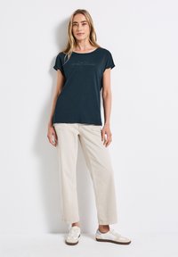 Mørkeblå kortærmet t-shirt med rund hals og trykt tekst på forsiden, parret med lysebeige vidde bukser og casual sneakers.