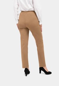 Tan stretchbroek met een elastische tailleband, met een slim fit en een gladde textuur, gecombineerd met zwarte hoge hakken.
