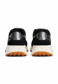 Zapatillas deportivas negras con parte superior de ante y malla, acentos reflectantes, mediopie en blanco y suela de goma texturizada con agarre naranja.