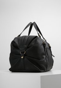Borsa a viaggio in pelle nera con forma arrotondata, doppi manici, chiusura con cerniera e dettagli in metallo dorato. Superficie con dettaglio testurizzato.