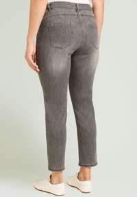 Jean en denim gris avec une coupe ajustée, poches arrière et ourlets retroussés, assorti à des baskets blanches pour un look décontracté.