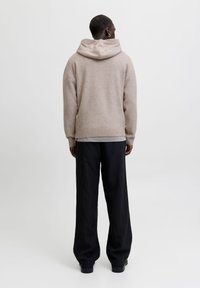 Sudadera con capucha beige y ribete en la parte inferior, hecha de un material suave, combinada con pantalones negros a rayas. Bajo contraste, diseño simple.