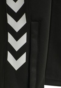 Schwarze Sporthose mit weißen Chevron-Streifen an den Seiten, aus dehnbarem Material mit glatter Oberfläche und Seitentaschen.