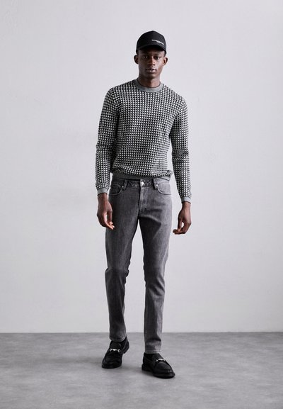 Un pull à motifs noir et blanc, un jean gris et des chaussures noires. La tenue présente un design texturé avec une silhouette ajustée.