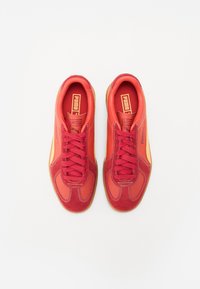 Baskets rouges avec un mélange de matériaux lisses et texturés. Elles disposent de lacets ronds, d'un col rembourré et d'une semelle en gomme. Détails en orange.