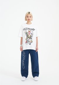 Vit oversized t-shirt med färggrafik från Ed Hardy som föreställer ett skalle och en orm. Kombinerad med mörkblå vida denimbyxor och vita sneakers.
