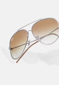 Óculos de sol aviador prateados com lentes castanhas em gradiente, armação em metal e almofadas de nariz transparentes. Tempos acentuados em castanho.