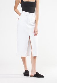 Hvid denim midi-nederdel med en frontslids, høj talje og bæltestropper. Sammen med sorte slip-on sko med korkdetalje.