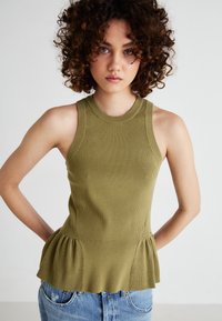 Olive roheline ribakudumine peplum-topp ümmarguse kaeluse ja ilma varrukateta disainiga, kombineeritud helesiniste kulunud teksadega.