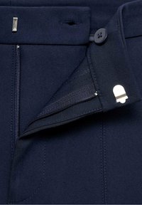 Primo piano di pantaloni blu navy che mostrano la zip, il bottone e la chiusura con gancio in metallo sulla vita.