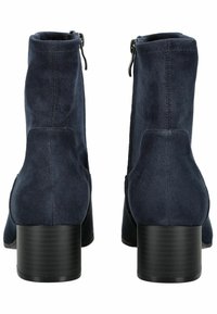 Une paire de bottines en nubuck bleu marine avec des talons blocs noirs et des zips à l'arrière, montrées de l'arrière sur fond blanc.