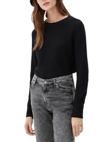 Femme portant un pull noir texturé à manches longues rentré dans un jean gris délavé taille haute avec poches avant, debout devant un fond blanc.