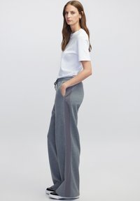 Grijze sweatpants met zijzakken en grijze zijstrepen, gecombineerd met een eenvoudig wit T-shirt. De stof lijkt zacht en ontspannen.
