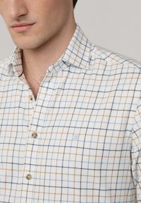 Camicia bianca con bottone, caratterizzata da un motivo a quadri con linee blu, marroni e azzurri. Include un piccolo logo ricamato e colletto standard.
